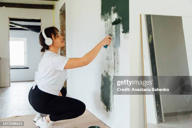 woman in head phones painting white wall in green color - decorator stock pictures, royalty-free photos & images