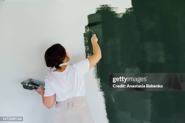 woman in head phones painting white wall in green color - dekorieren stock-fotos und bilder