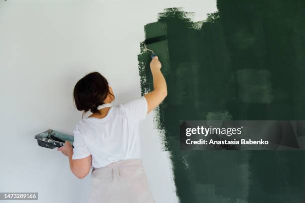 woman in head phones painting white wall in green color - malen lackieren stock-fotos und bilder