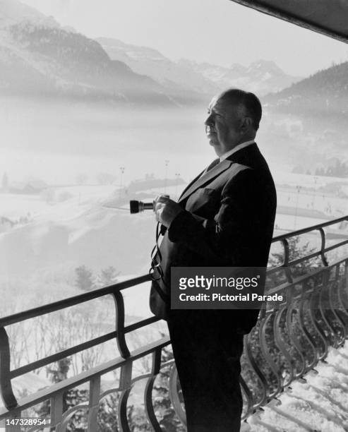 English film director director Alfred Hitchcock holding a camera as he admires the view from his balcony during a holiday in St Moritz, Switzerland,...