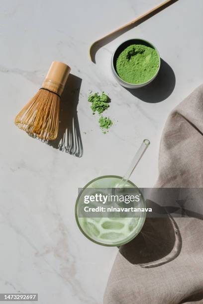 overhead view of a glass of iced matcha drink, bamboo whisk, matcha powder, matcha spoon and napkin - foodstyling stock-fotos und bilder