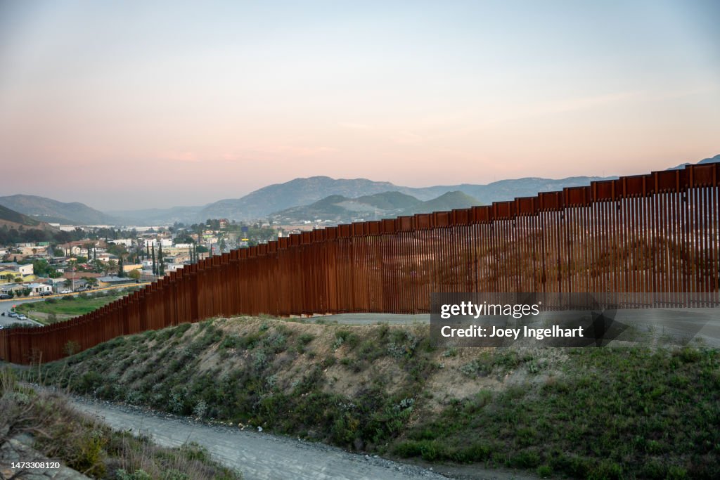 Internationale Grenzmauer zwischen Tecate California und Tecate Mexico bei Tijuana Baja California Norte in der Abenddämmerung unter atemberaubendem Sonnenuntergang mit Blick auf die Stadt aus den USA