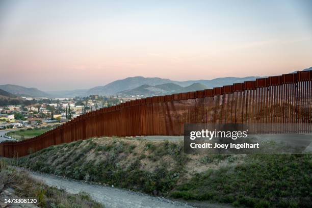 internationale grenzmauer zwischen tecate california und tecate mexico bei tijuana baja california norte in der abenddämmerung unter atemberaubendem sonnenuntergang mit blick auf die stadt aus den usa - internationale grenze stock-fotos und bilder