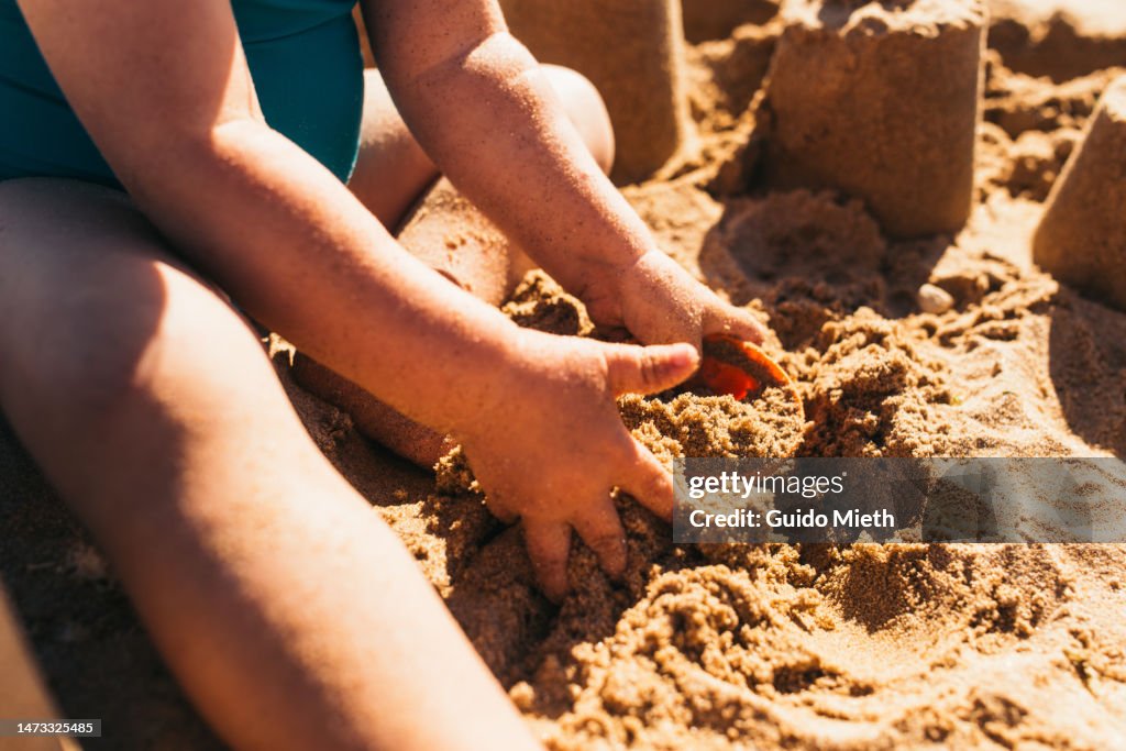 Toddler girl playing with a bucket in the sand of a beach.