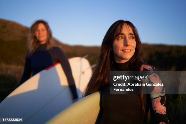 happy women in wetsuit and carrying surfboards to the beach - passenger train stockfoto's en -beelden