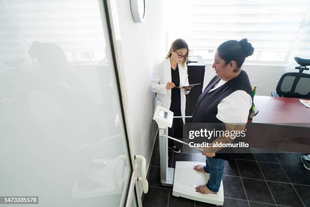 overweight latin woman standing on weighing scale - doctor's office scale stock pictures, royalty-free photos & images