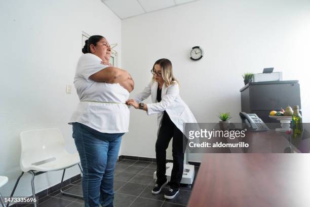 female nutritionist using measuring tape around overweight woman - woman measuring tape stock pictures, royalty-free photos & images