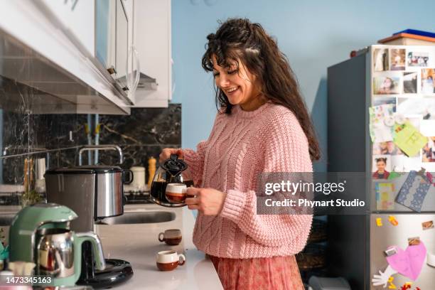 lächelnde frau gießt kaffee in eine tasse - kaffeemaschine stock-fotos und bilder