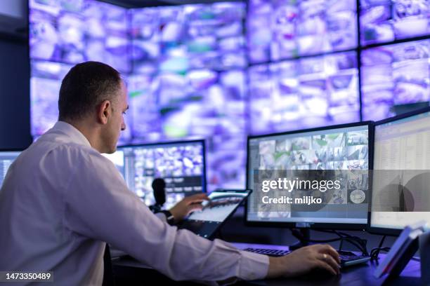uomo che lavora nella stanza di sorveglianza e guarda i monitor - sorveglianza foto e immagini stock
