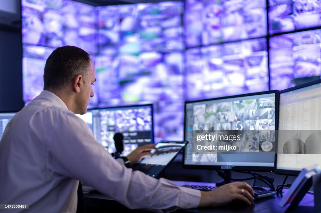 Homem trabalhando na sala de vigilância e olhando para monitores