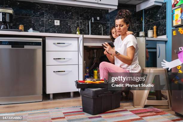 frau, die versucht, klempnerreparatur durch online-lern-tutorial zu reparieren - wasserschaden stock-fotos und bilder