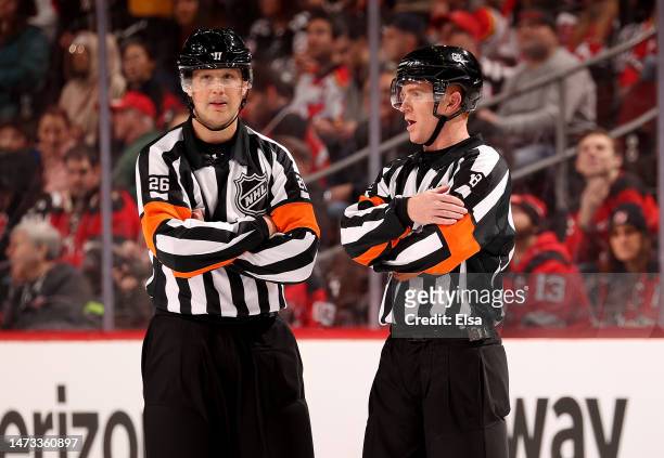 Referees Jacob Brenk and Tom Chmielewski talk during a stop in play in the first period between the New Jersey Devils and the Carolina Hurricanes at...