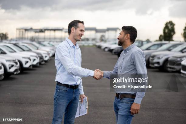 salesman handshaking with a client after buying a car at the dealership - fleet stockfoto's en -beelden