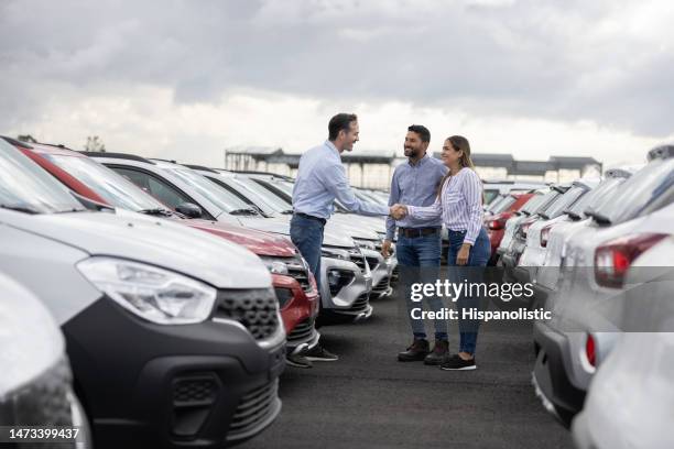 couple handshaking with a car salesperson after buying a car - car showroom stock pictures, royalty-free photos & images