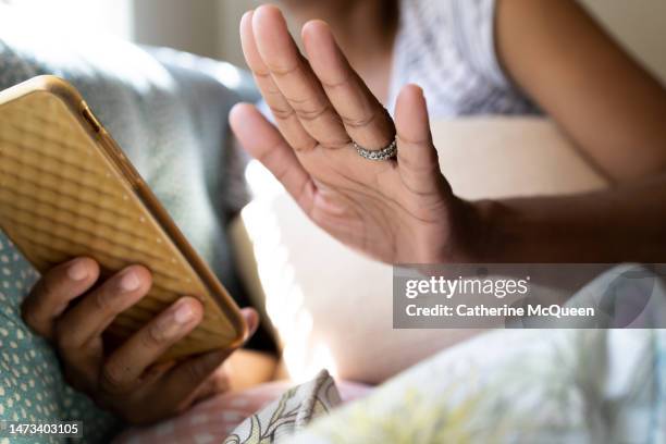 mid adult black woman holding hand up while using smart phone sitting on sofa - geste stop photos et images de collection