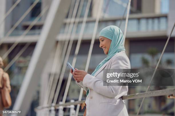 muslim woman, phone and smile in the city for social media, communication or chatting on bridge outdoors. happy islamic female employee with hijab smiling on smartphone for 5g connection in dubai - dubai bridge stock pictures, royalty-free photos & images