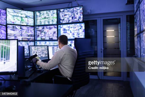 hombre trabajando en sala de vigilancia y mirando monitores - servizio fotografico fotografías e imágenes de stock