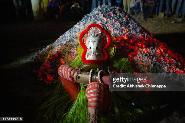 Man dressed in the likeness of the Hindu deity Pottan lies on burning cinders of coal as he performs during the Theyyam ritualistic dance festival on...