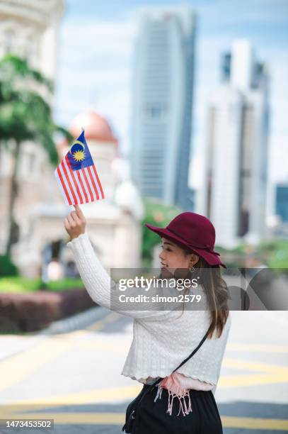 in a display of national pride, a young female tourist waves the malaysian flag at merdeka square in kuala lumpur, malaysia - malaysia kuala lumpur merdeka square stock pictures, royalty-free photos & images