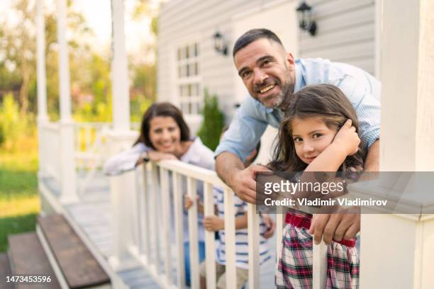 zwei eltern kuscheln kleine tochter und kleinen sohn draußen auf der veranda - eigenheim familie stock-fotos und bilder