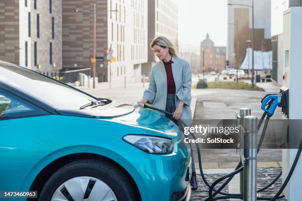 businesswoman charging at fast charge point - elektrische auto stockfoto's en -beelden