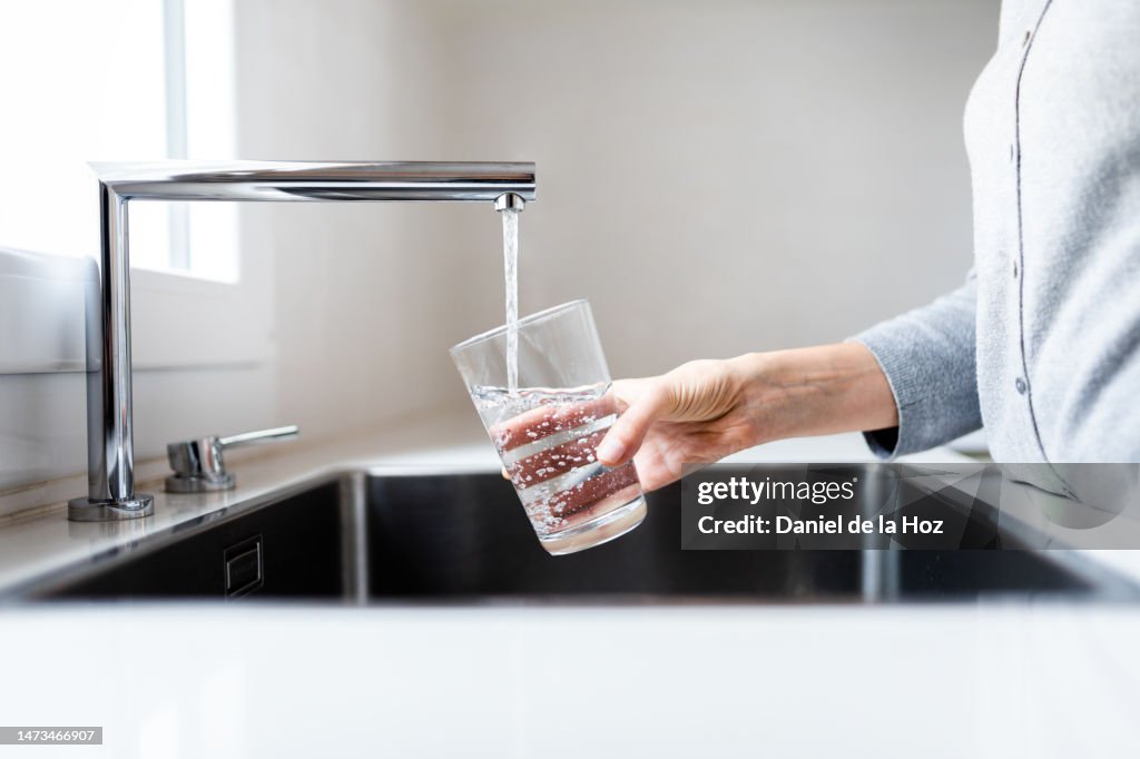Unrecognizable thirsty woman filling drinking glass with water to drink. Stay hydrated.