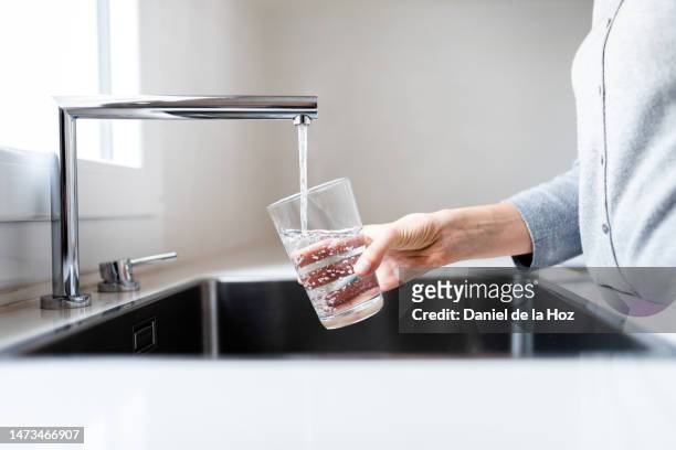 unrecognizable thirsty woman filling drinking glass with water to drink. stay hydrated. - zapfen stock-fotos und bilder