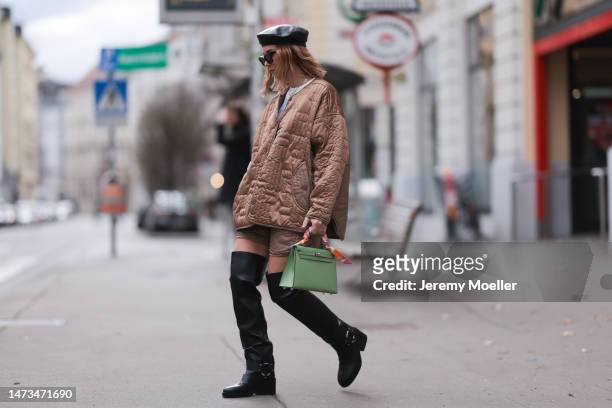 Karin Teigl seen wearing Rhude black sunglasses, Marc Cain black leather beret hat, gold / silver rings, Munthe brown quilted jacket and matching...