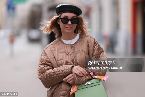 Karin Teigl seen wearing Rhude black sunglasses, Marc Cain black leather beret hat, gold / silver rings, Munthe brown quilted jacket, Hermès light...