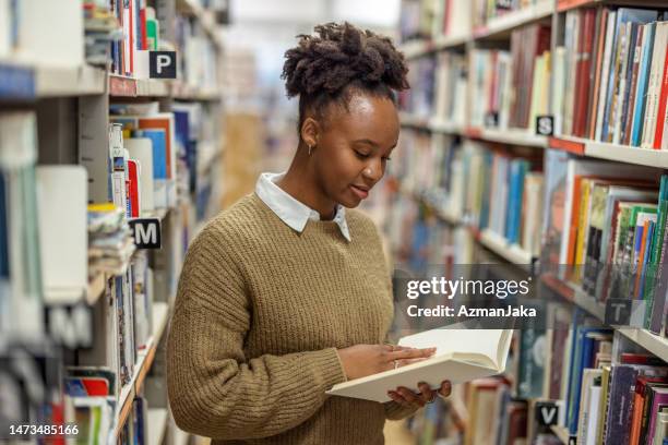 young african-american student reading a book in the library - college library stock pictures, royalty-free photos & images