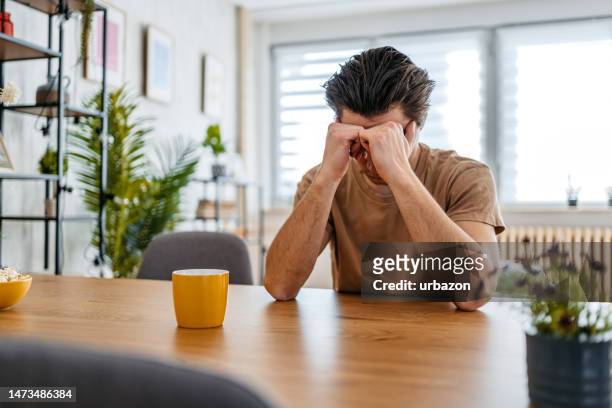 joven triste sentado en casa en la mesa de la cocina - hopelessness fotografías e imágenes de stock