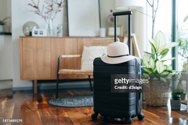 still life of a black suitcase with a straw hat in the living room of an apartment. travel and vacation concept - vakantiehuis stockfoto's en -beelden