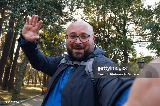 a man, a blogger, making a video call using a smartphone camera, standing on a city street of a european city. a happy man, a tourist with a mobile phone in his hands. video broadcast, communication with friends, family. maintaining social networks. - mensaje de móvil fotografías e imágenes de stock