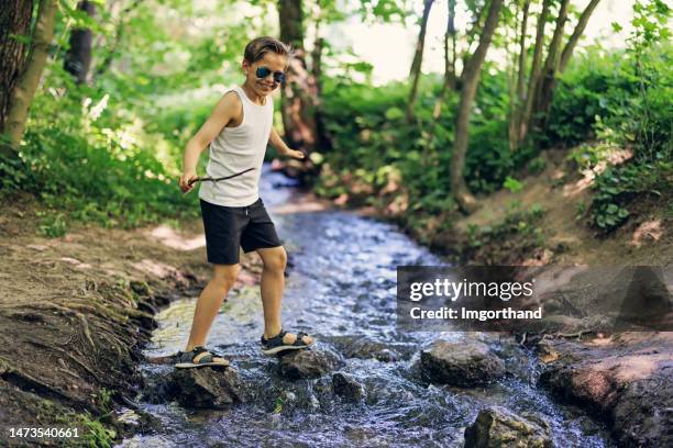 teenage boy is walking through stream in forest. - boy river looking at camera stock pictures, royalty-free photos & images