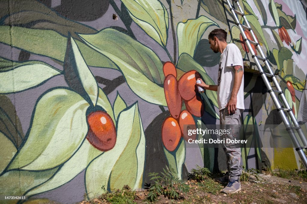 Un artista di graffiti dipinge graffiti su un grande muro di contenimento.