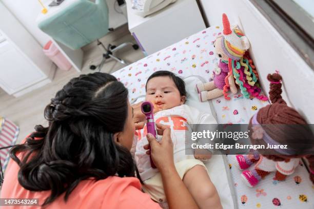 doctora pediatra revisando la boca de un bebe con un otoscopio, que esta acostado en la cama del hospital - acostado stock pictures, royalty-free photos & images