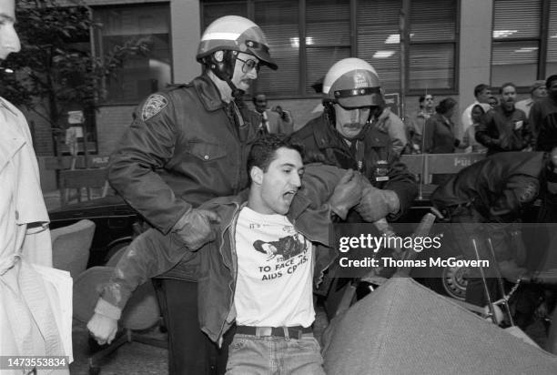 Two police officers arresting an AIDS protestor chained to a chair at the New York City Department of Social Services in 1989 in New York City in New...
