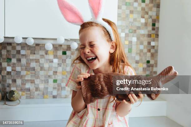 red head girl wearing bunny ears, holding chocolate bunny and laughing - chocolate bunny stock-fotos und bilder