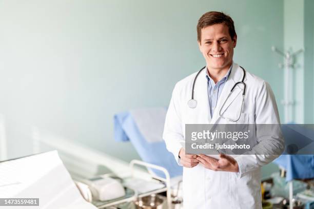 jovem médico sorridente em pé em seu consultório e usando tablet digital - visão geral - fotografias e filmes do acervo