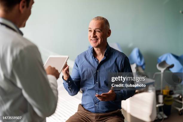 doctor in surgery with male patient using digital tablet - mature men talking stock pictures, royalty-free photos & images