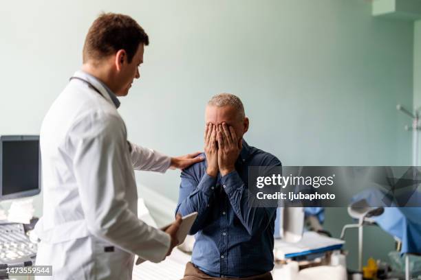 un médecin parle à un patient masculin malheureux dans la salle d’examen - blouse dexamen médical photos et images de collection