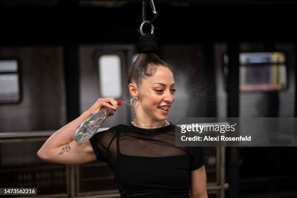 Aerialist Erin Blaire sprays her hair with water before performing a hair hanging trick for a photographer on a subway platform on March 14, 2023 in...