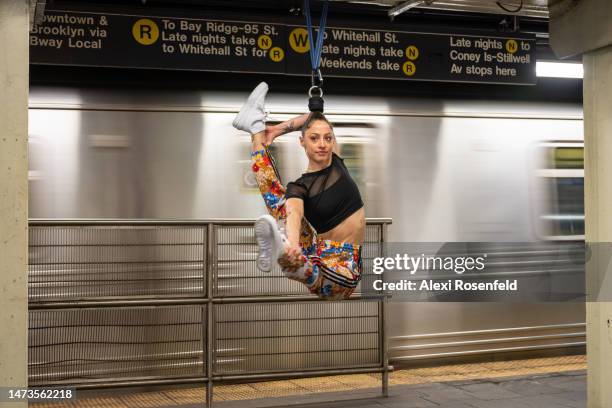 Aerialist Erin Blaire performs a hair hanging trick for a photographer while hanging from a metal bar on a subway platform on March 14, 2023 in New...