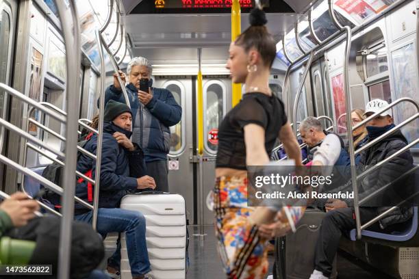 People watch as aerialist Erin Blaire performs hair hanging tricks for a photographer and commuters while hanging from the overhead hand-rails on a...