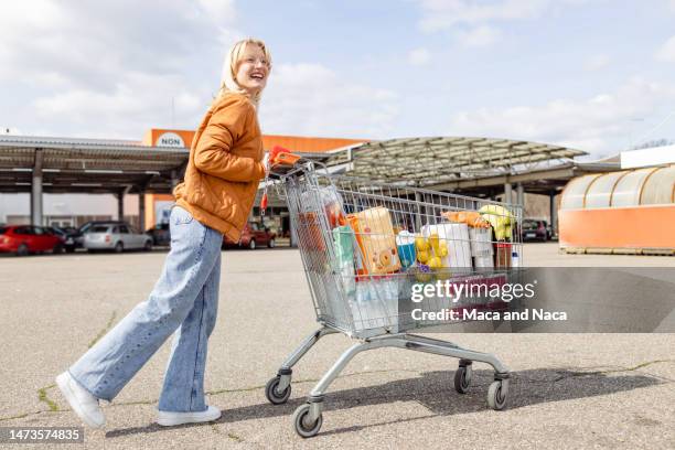 junge frau, die spaß daran hat, einen einkaufswagen zu schieben - shopping cart stock-fotos und bilder
