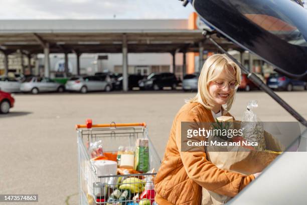 woman putting groceries in her car on a parking lot - oranges in basket at food market stock pictures, royalty-free photos & images