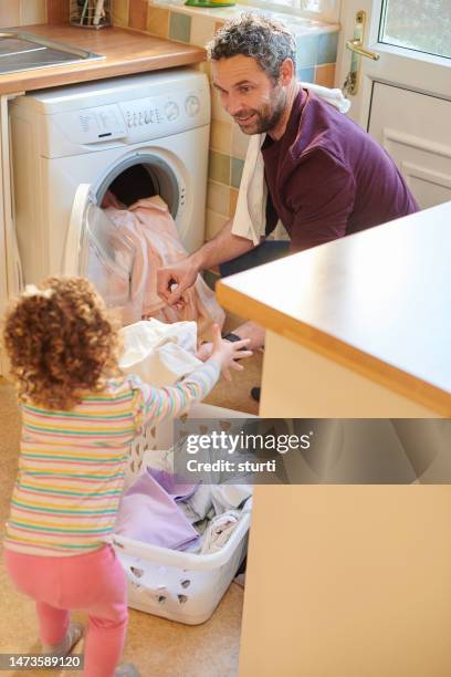 dad and daughter loading the washing machine - man washing basket child stock pictures, royalty-free photos & images