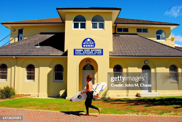 surfer runs past bondi surf bathers life saving club, bondi beach (australia) - surf life saving stockfoto's en -beelden