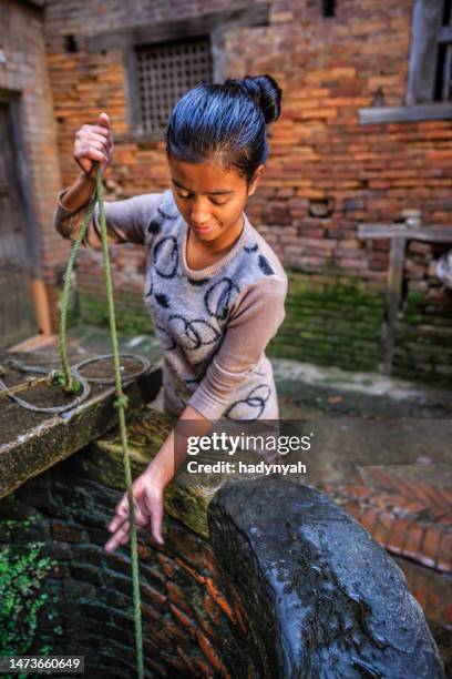 joven chica nepali primeros agua de un bien de bhaktapur - pozo agua fotografías e imágenes de stock