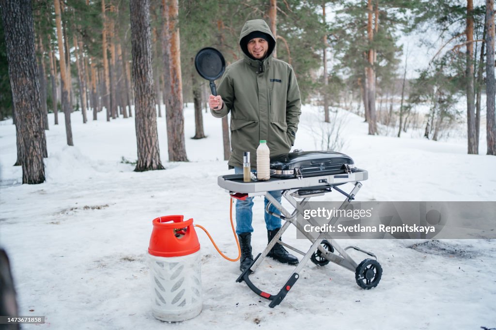 Man fries pancakes on a gas grill in a snowy forest in the spring picnic